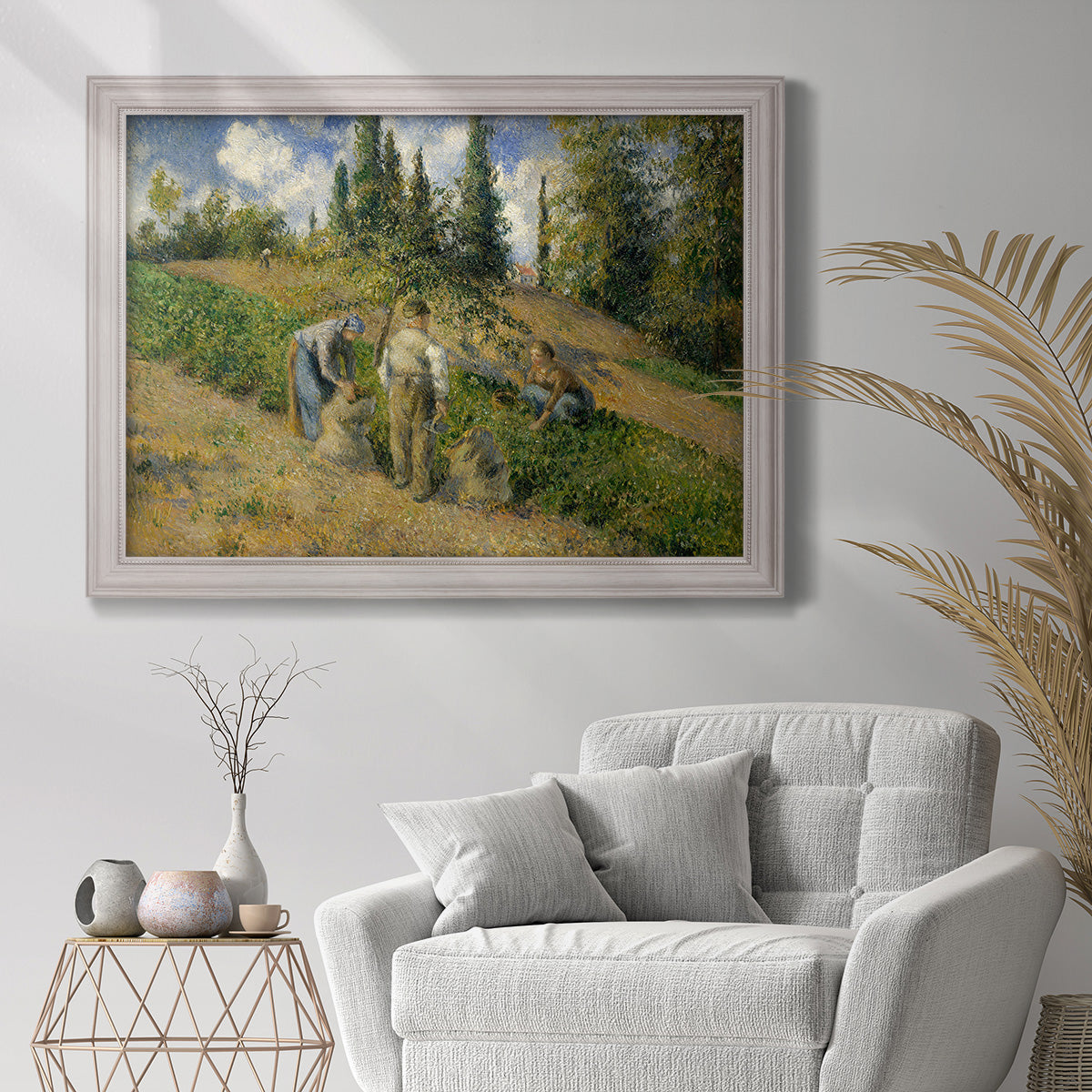 Impressionist countryside harvest scene by Camille Pissarro in an ornate weathered white frame displayed in a bright interior setting.