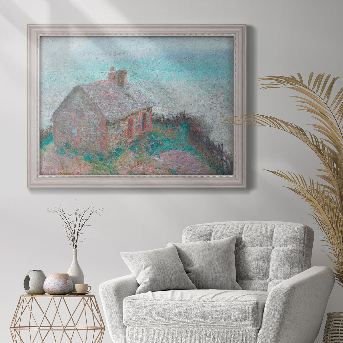 Impressionist coastal building landscape by Claude Monet in an ornate weathered white frame displayed in a bright interior setting.