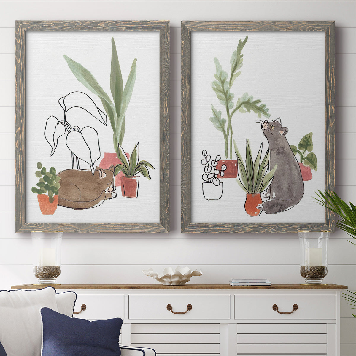 Set of two gray barnwood framed canvas prints depicting a coordinated art pair of cats tucked among collections of potted houseplants rendered as whimsical botanical animal illustrations above a dining room sideboard.