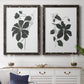 Set of two black barnwood framed canvas prints depicting a coordinated art pair of black leafy vine silhouettes rendered as minimalist botanical prints above a dining room sideboard.