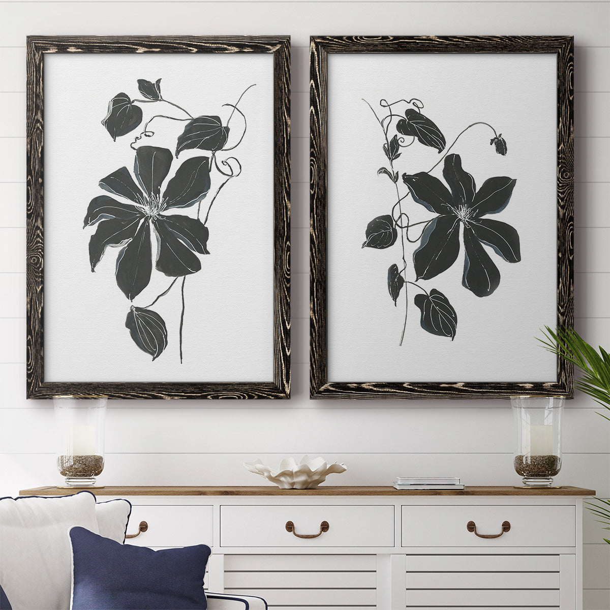 Set of two black barnwood framed canvas prints depicting a coordinated art pair of black leafy vine silhouettes rendered as minimalist botanical prints above a dining room sideboard.