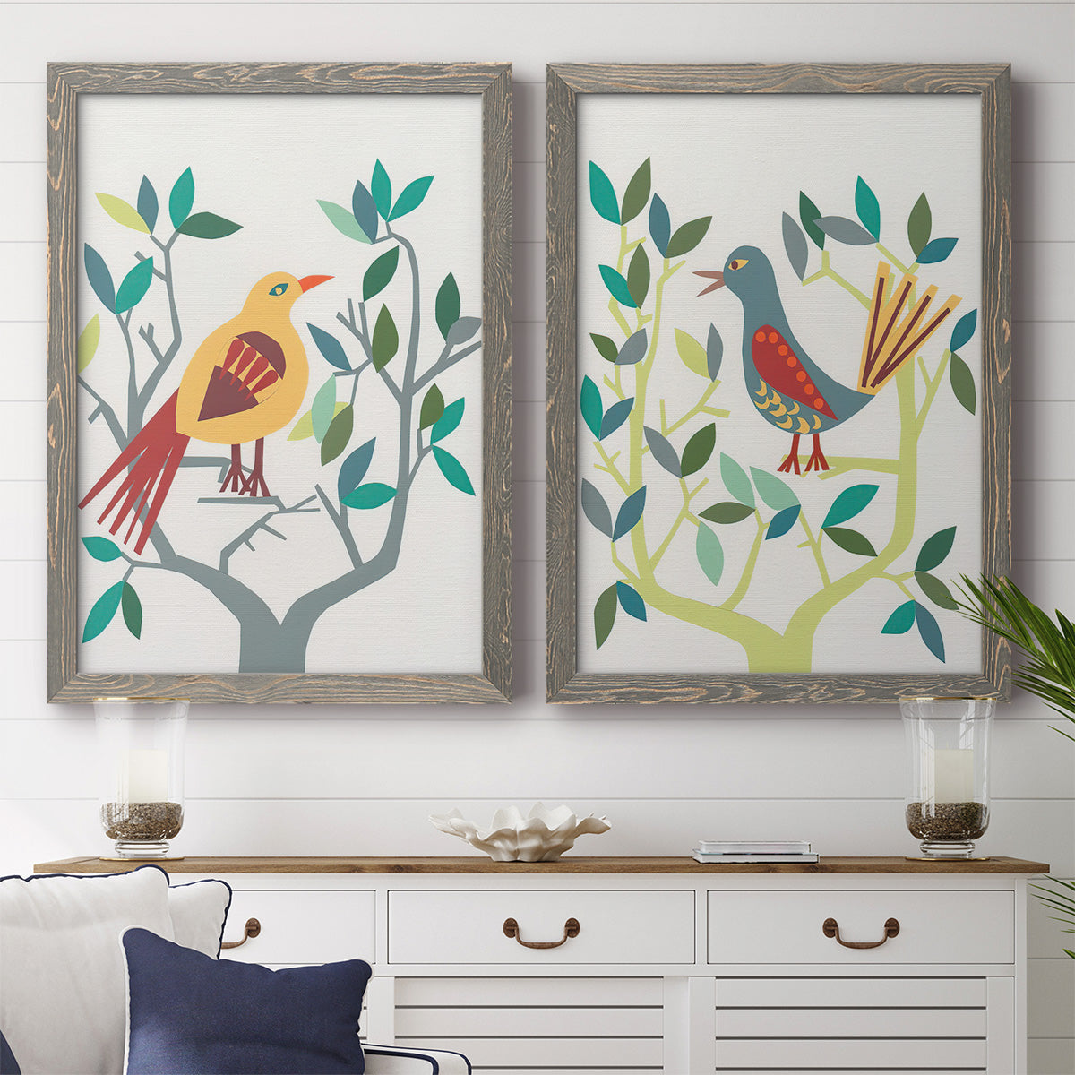 Set of two gray barnwood framed canvas prints depicting a coordinated art pair of stylized colorful birds perched among leafy branches rendered as modern folk-art bird illustrations above a dining room sideboard.