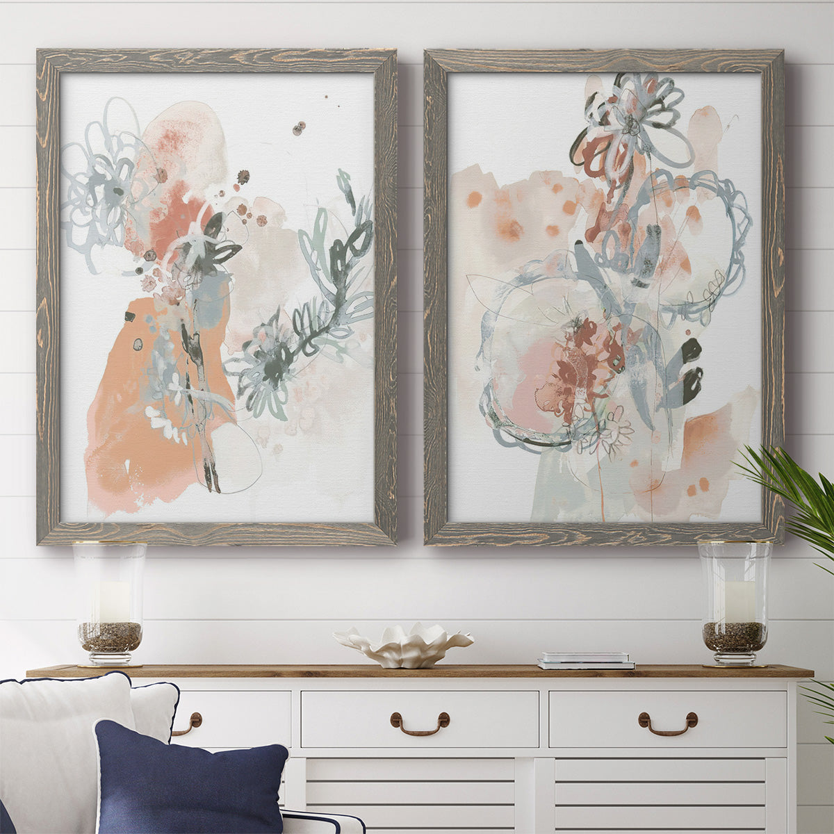 Set of two gray barnwood framed canvas prints depicting a coordinated art pair of loose blush gray and coral floral gestures rendered as abstract watercolor botanicals above a dining room sideboard.