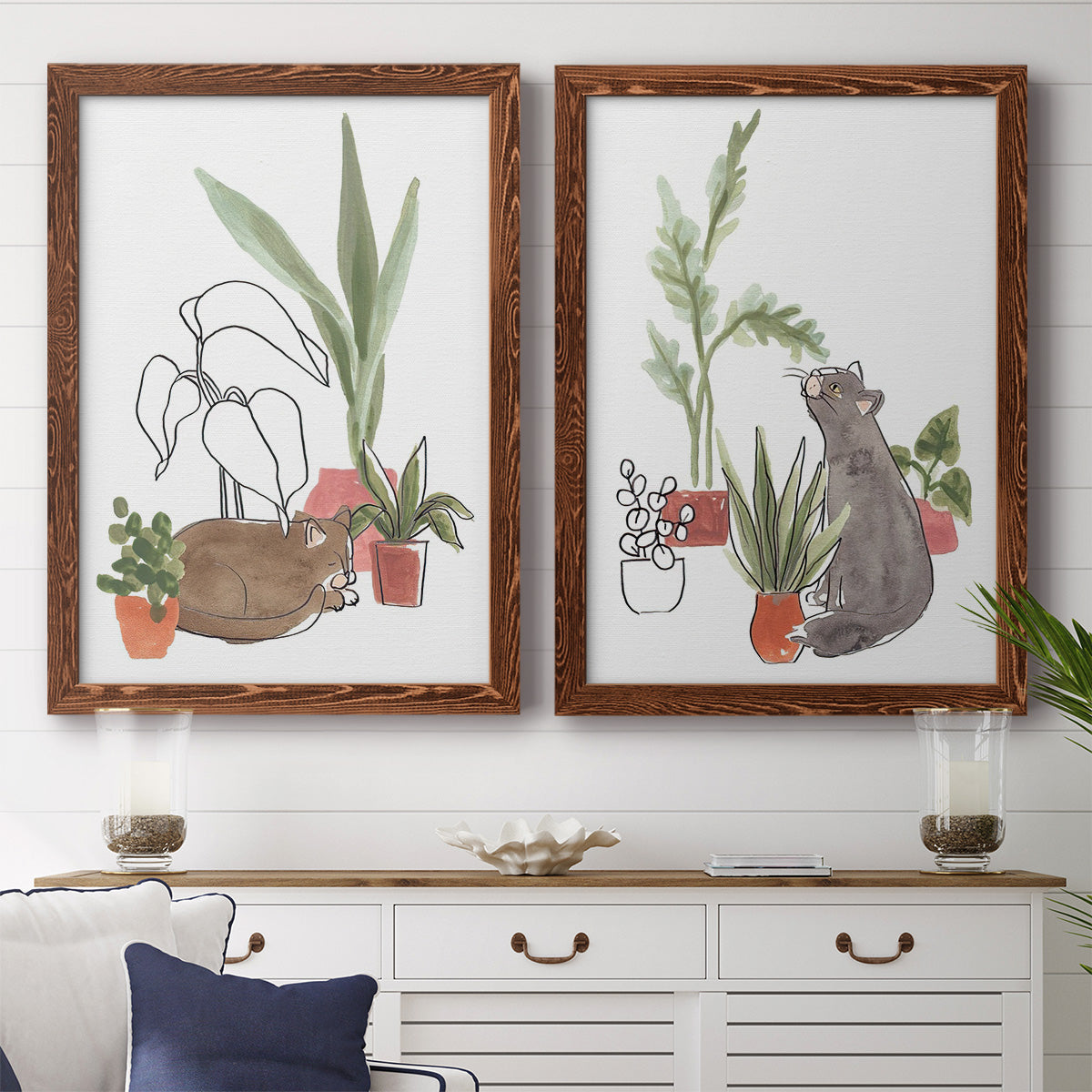 Set of two maple barnwood framed canvas prints depicting a coordinated art pair of cats tucked among collections of potted houseplants rendered as whimsical botanical animal illustrations above a dining room sideboard.