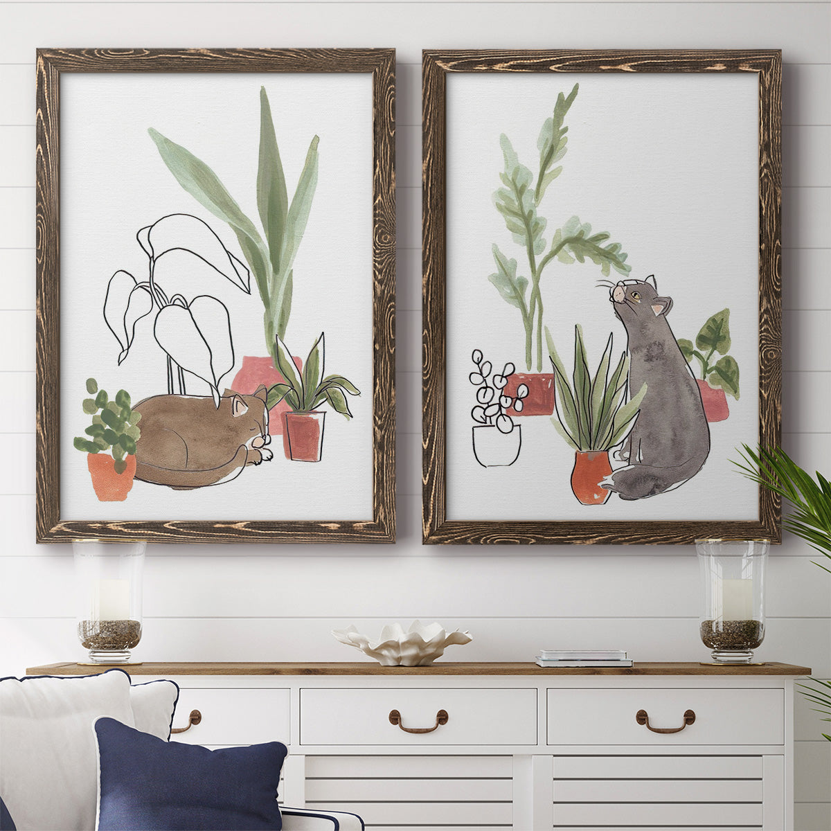 Set of two walnut barnwood framed canvas prints depicting a coordinated art pair of cats tucked among collections of potted houseplants rendered as whimsical botanical animal illustrations above a dining room sideboard.
