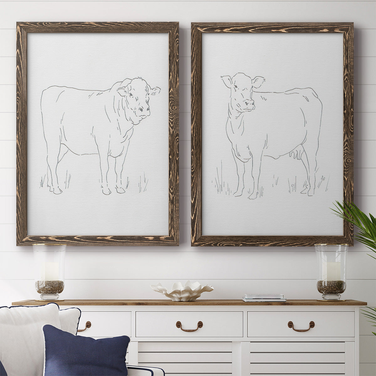 Set of two walnut barnwood framed canvas prints depicting a coordinated art pair of simple contour drawings of standing cows rendered as minimalist livestock sketches above a dining room sideboard.