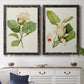 Set of two black barnwood framed canvas prints depicting a coordinated art pair of white magnolia blossoms and glossy green leaves rendered as traditional botanical paintings above a dining room sideboard.