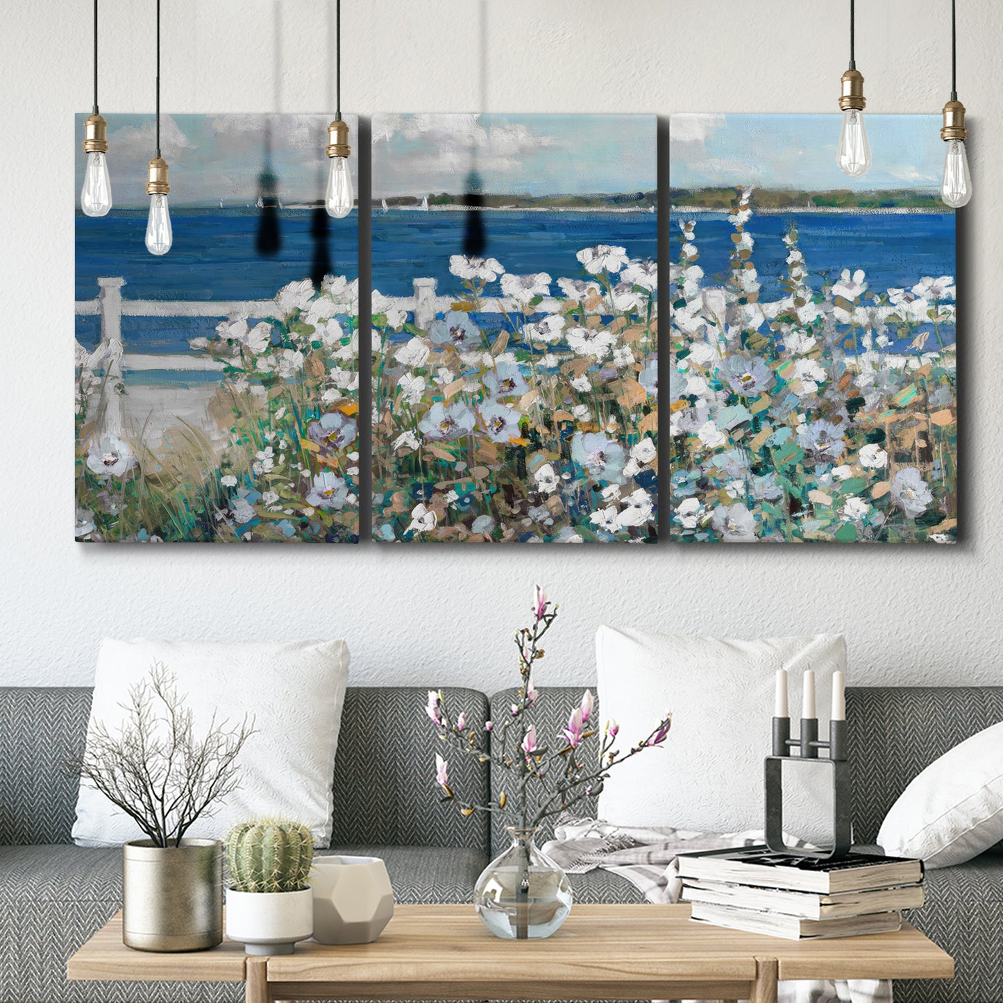 Three-panel canvas wall art featuring coastal garden overlooking bay, displayed in a modern living room above seating.