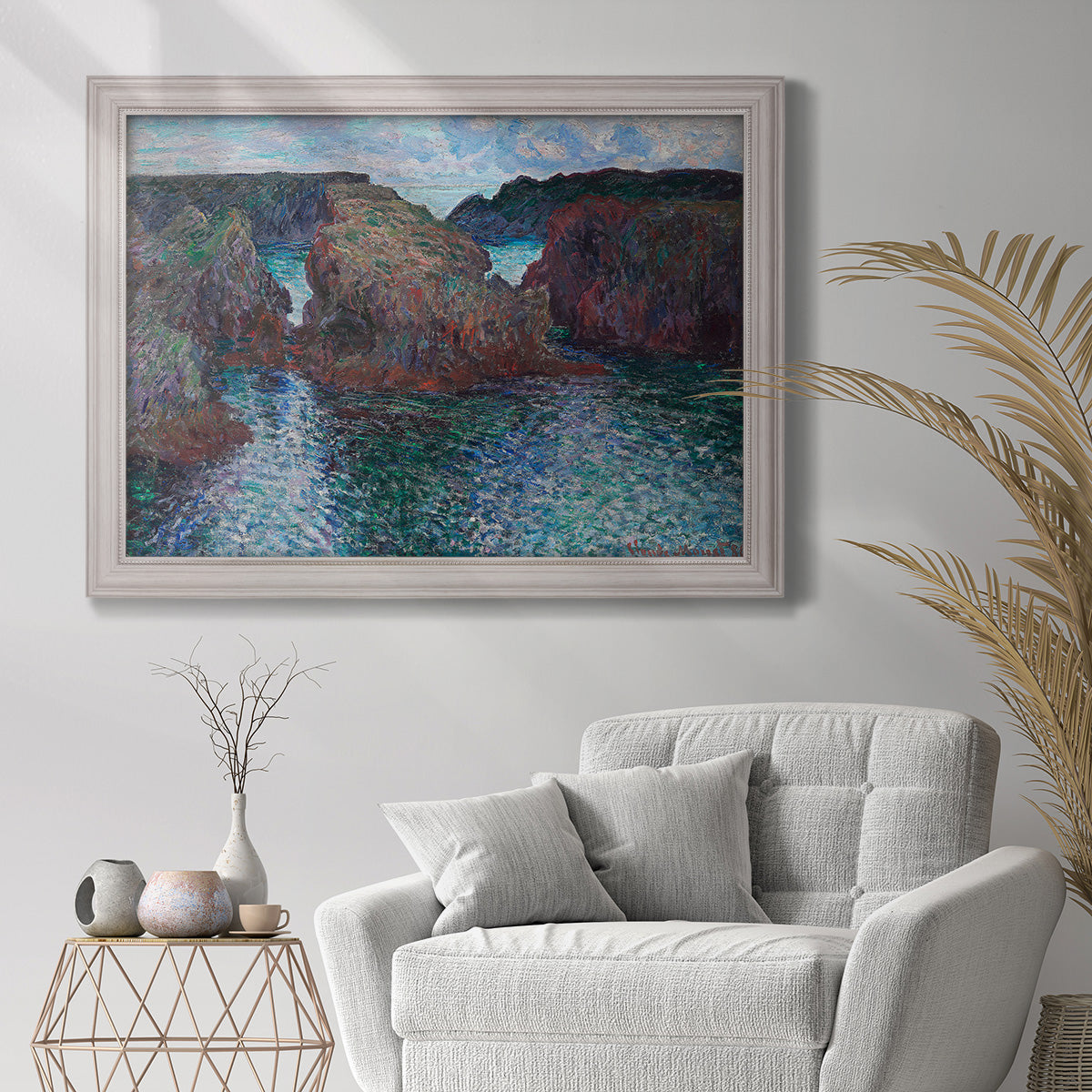 Impressionist rocky seascape by Claude Monet in an ornate weathered white frame displayed in a bright interior setting.
