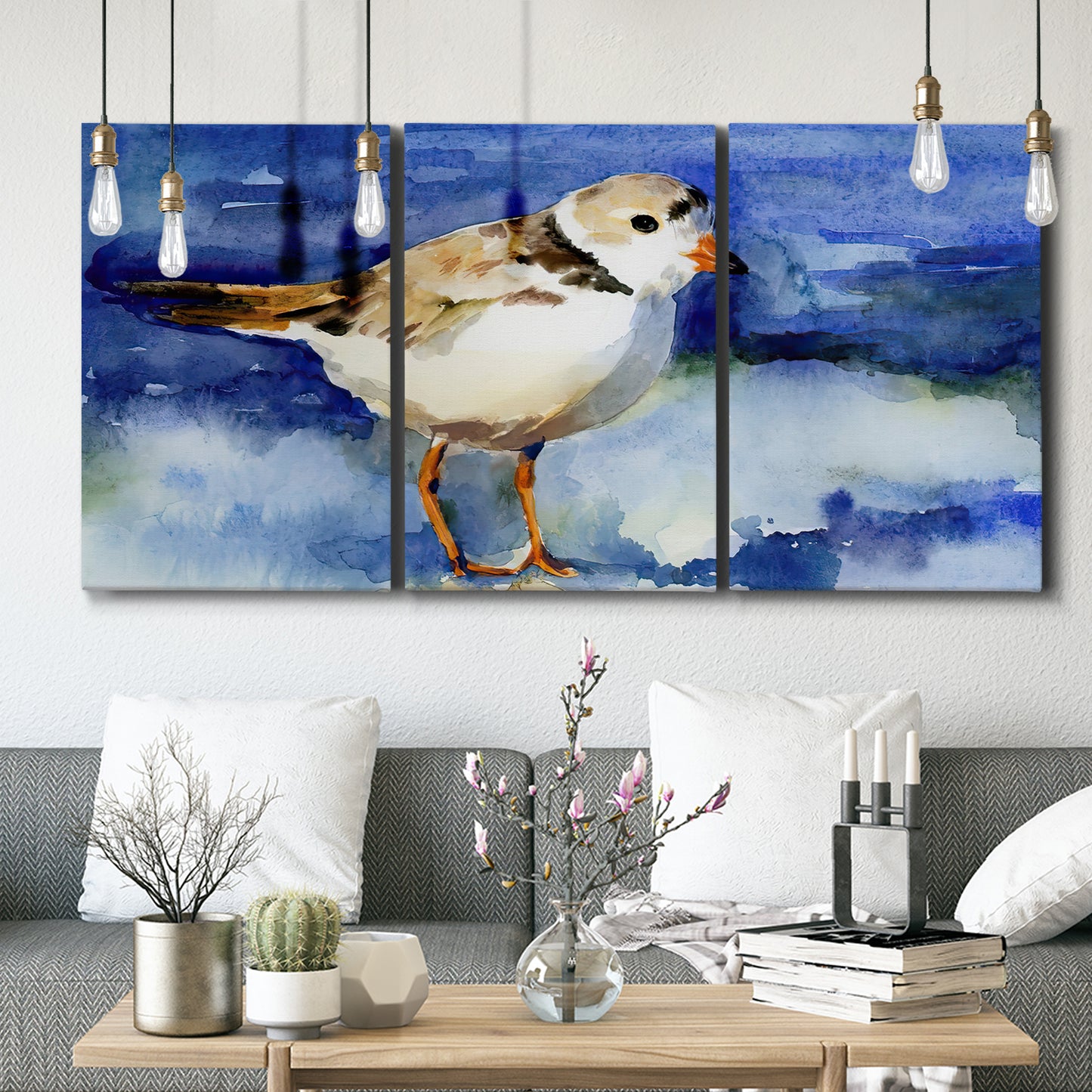 Three-panel canvas wall art featuring shorebirds standing in shallow water, displayed in a modern living room above seating.