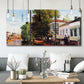 Three-panel canvas wall art featuring riverside houses along canal, displayed in a modern living room above seating.