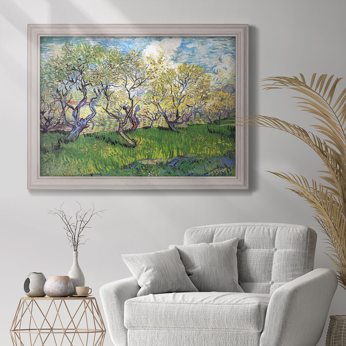 Impressionist spring orchard landscape by Vincent van Gogh in an ornate weathered white frame displayed in a bright interior setting.