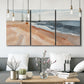 Three-panel canvas wall art featuring abstract coastal beach composition, displayed in a modern living room above seating.