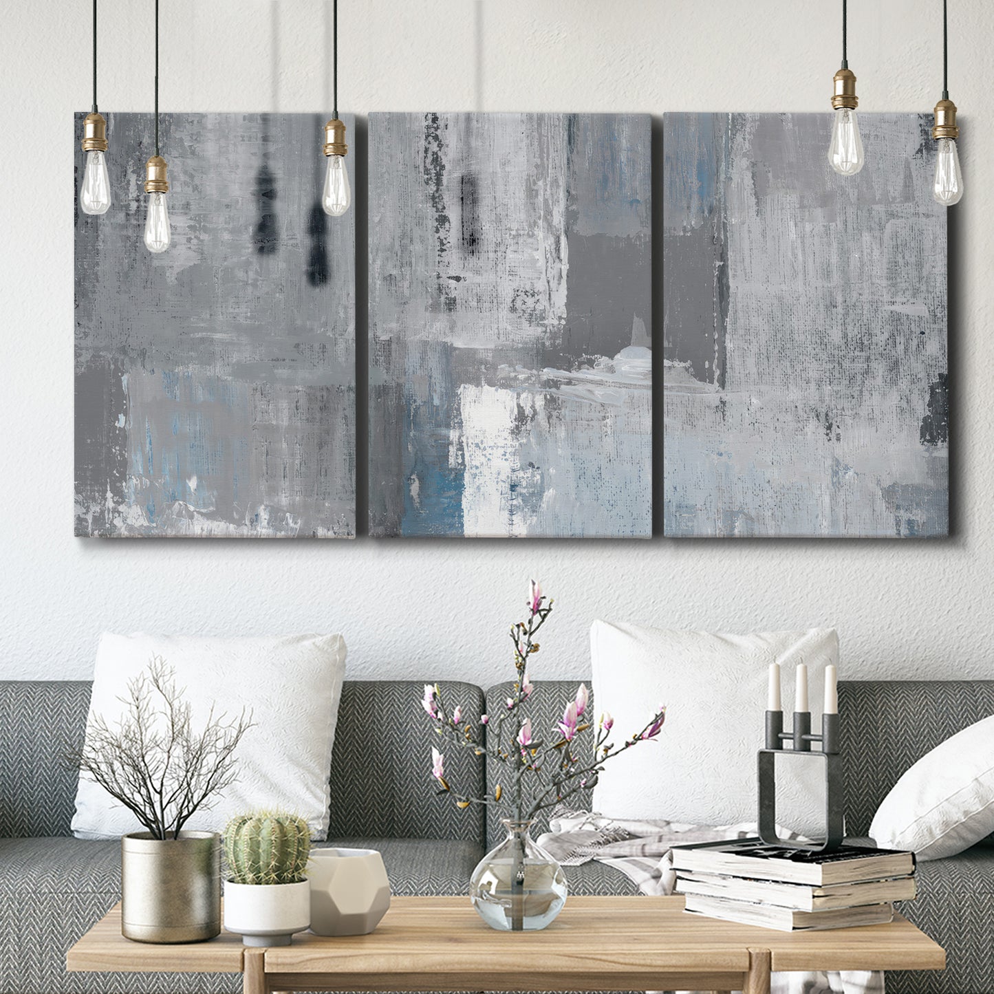 Three-panel canvas wall art featuring cool toned industrial abstract blues, displayed in a modern living room above seating.