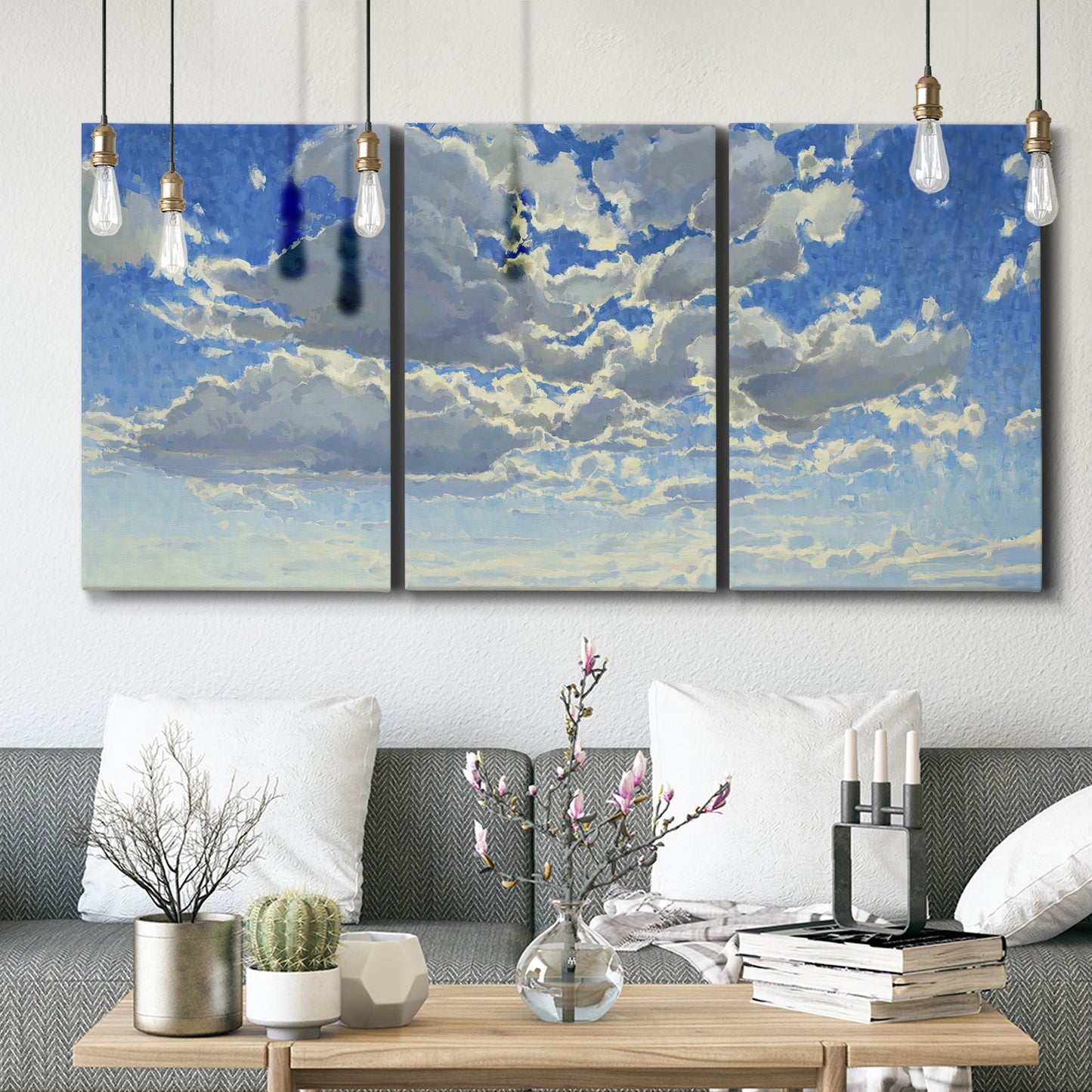 Three-panel canvas wall art featuring whimsical cloud filled sky landscape, displayed in a modern living room above seating.