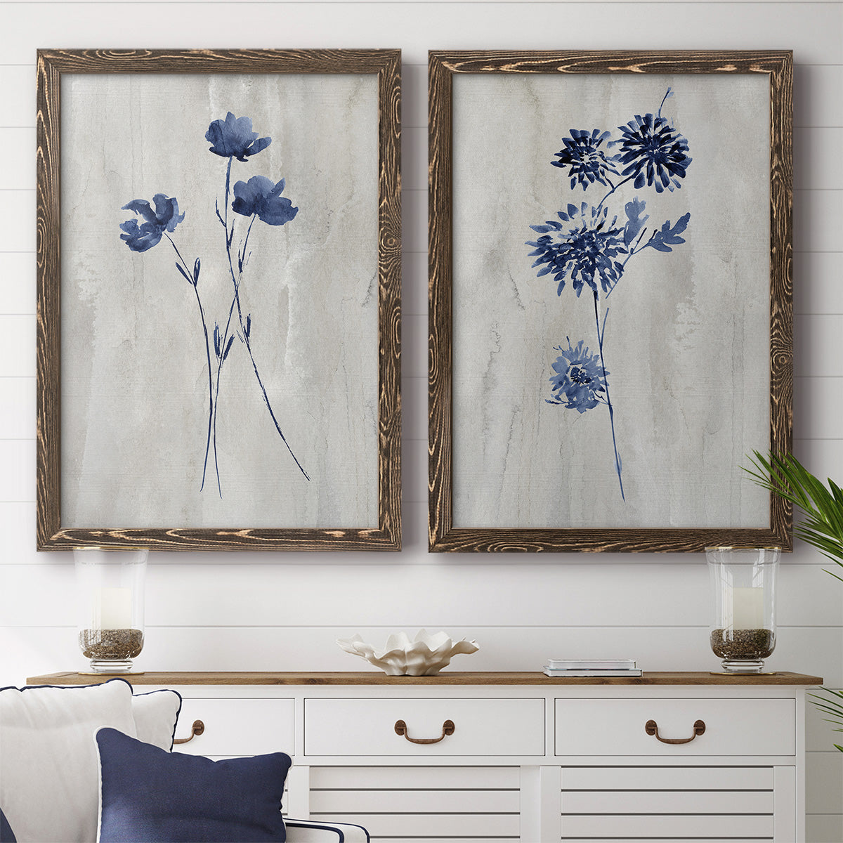 Set of two walnut barnwood framed canvas prints depicting a coordinated art pair of blue wildflower stems on weathered neutral paper rendered as rustic monochrome botanical paintings above a dining room sideboard.