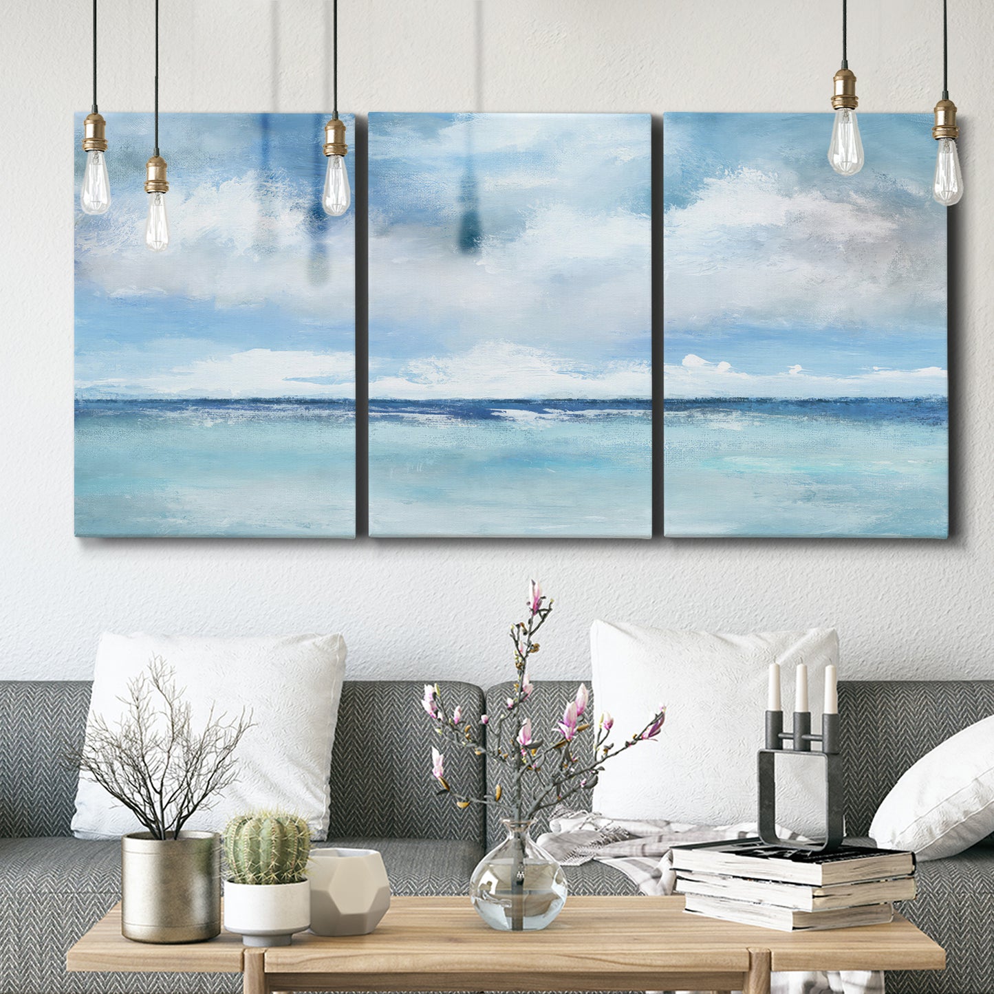 Three-panel canvas wall art featuring tropical clouds over ocean horizon, displayed in a modern living room above seating.