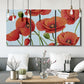 Three-panel canvas wall art featuring red poppies in motion, displayed in a modern living room above seating.