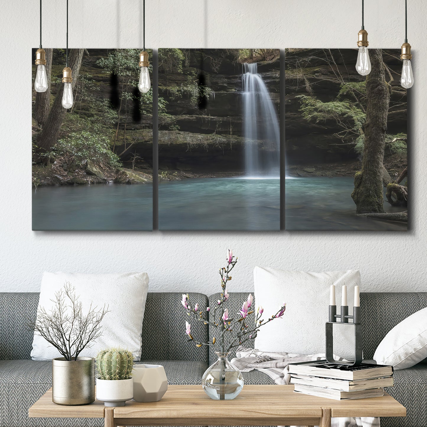 Three-panel canvas wall art featuring waterfall cascading through forest, displayed in a modern living room above seating.