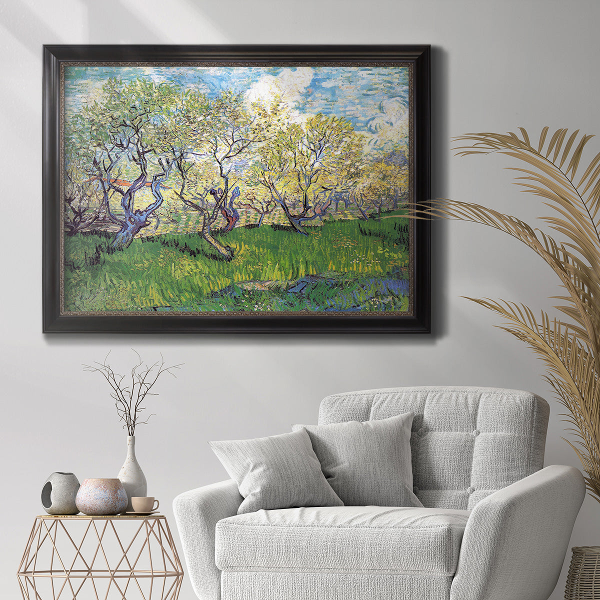 Impressionist spring orchard landscape by Vincent van Gogh in an ornate black frame with gilded inner detail displayed in a bright interior setting.