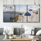 Three-panel canvas wall art featuring white buildings overlooking sea cliffs, displayed in a modern living room above seating.