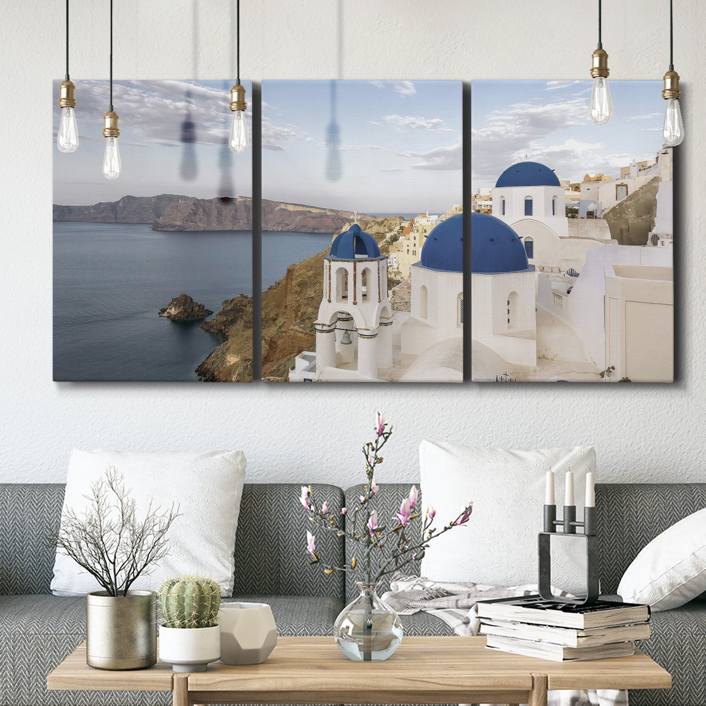 Three-panel canvas wall art featuring white buildings overlooking sea cliffs, displayed in a modern living room above seating.