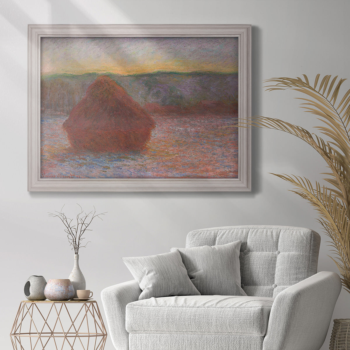 Impressionist haystack sunset scene in winter by Claude Monet in an ornate weathered white frame displayed in a bright interior setting.