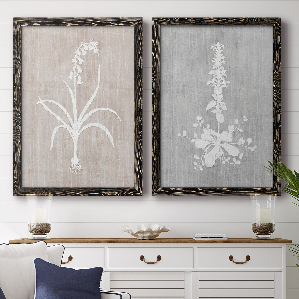 Set of two black barnwood framed canvas prints depicting a coordinated art pair of white botanical silhouettes on softly weathered neutral backgrounds rendered as rustic minimalist botanical prints above a dining room sideboard.