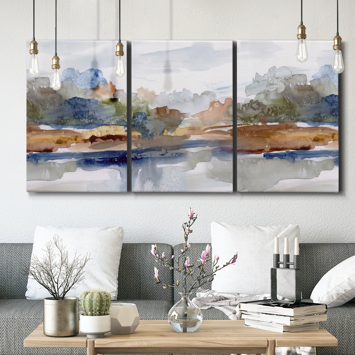 Three-panel canvas wall art featuring layered abstract mountain forms, displayed in a modern living room above seating.