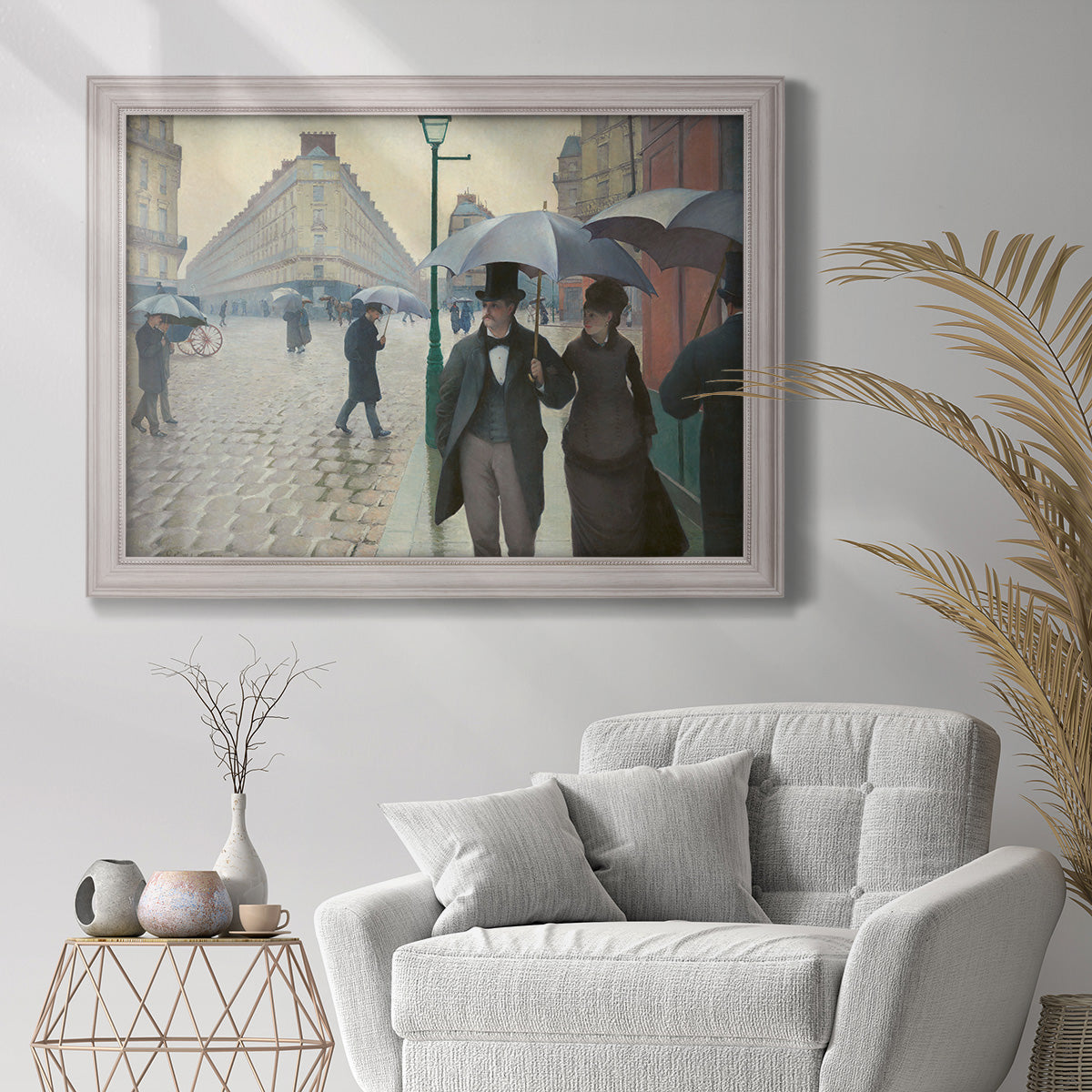 Impressionist urban street scene in the rain by Gustave Caillebotte in an ornate weathered white frame displayed in a bright interior setting.