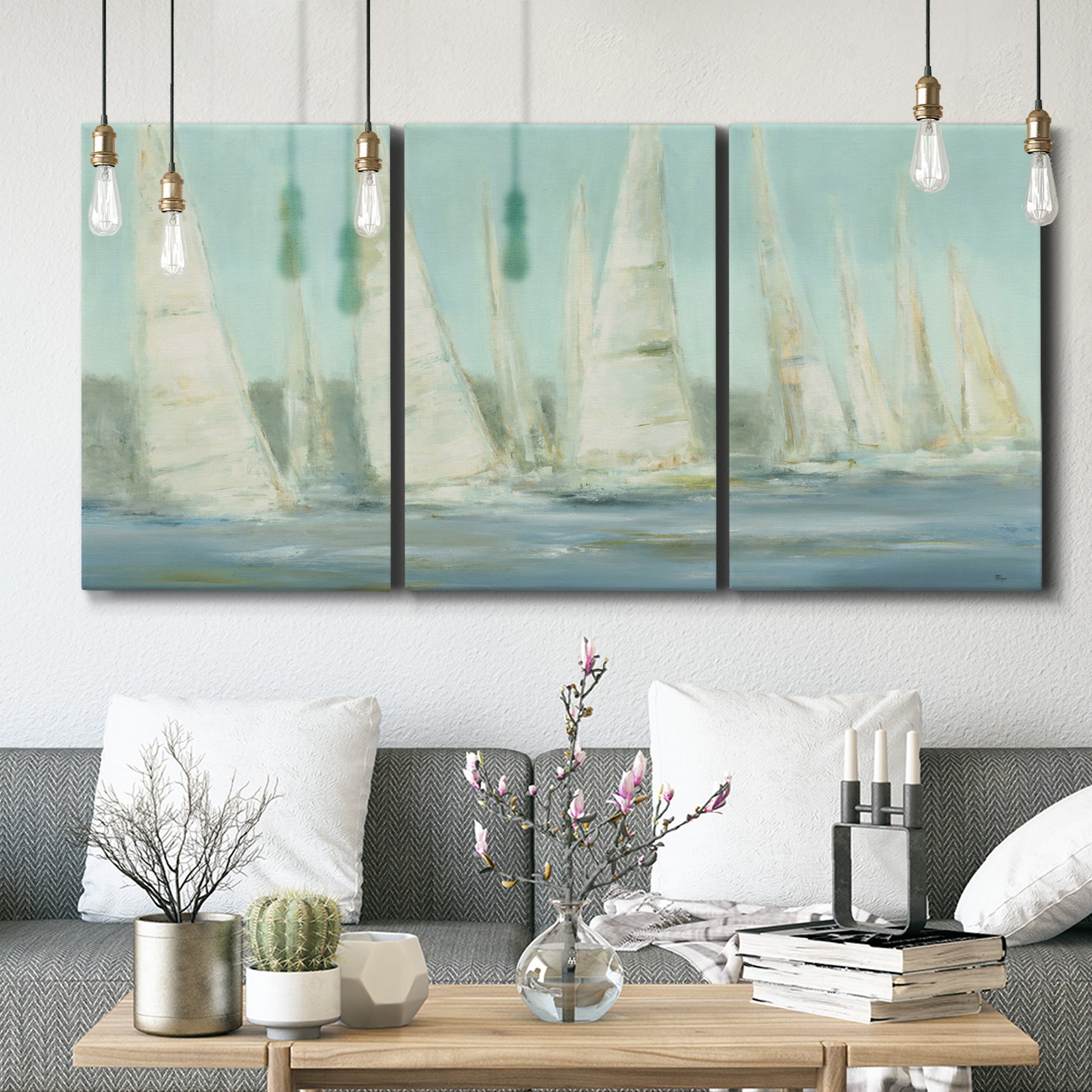 Three-panel canvas wall art featuring sailboats silhouetted at sunrise, displayed in a modern living room above seating.