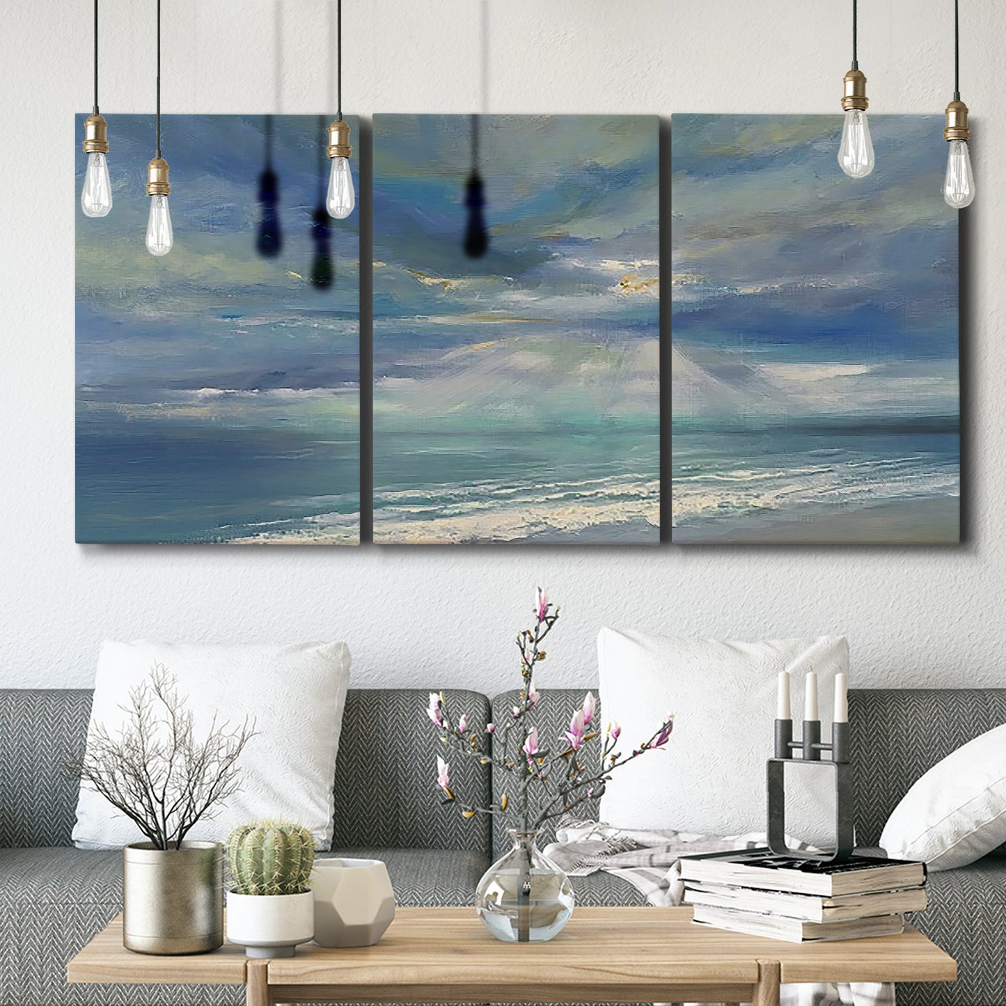 Three-panel canvas wall art featuring sunbeams breaking through coastal clouds, displayed in a modern living room above seating.