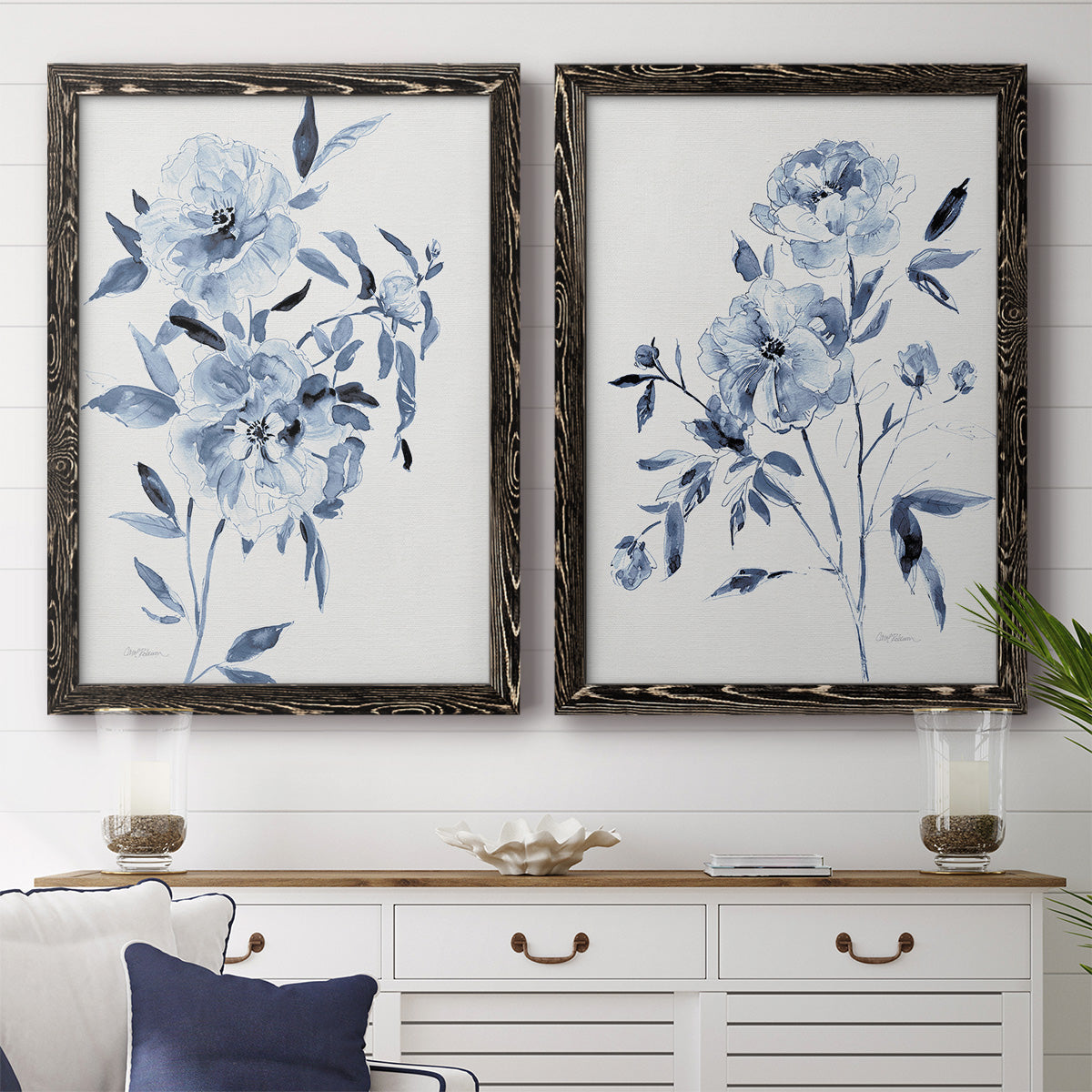 Set of two black barnwood framed canvas prints depicting a coordinated art pair of loose blue flowers and leafy branches rendered as expressive watercolor botanical paintings above a dining room sideboard.
