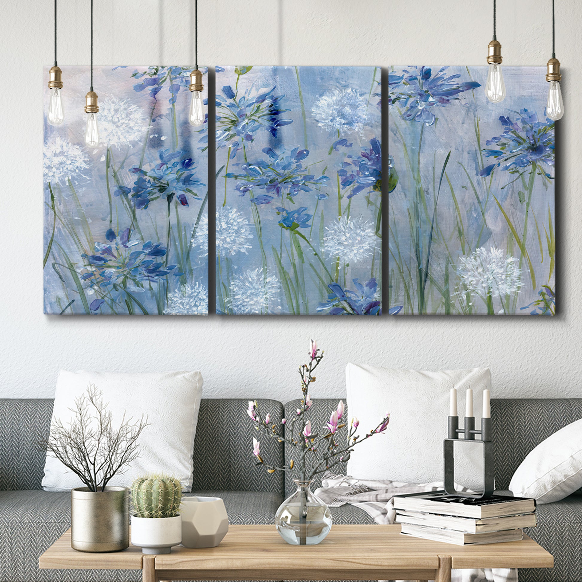 Three-panel canvas wall art featuring delicate watercolor floral blooms, displayed in a modern living room above seating.