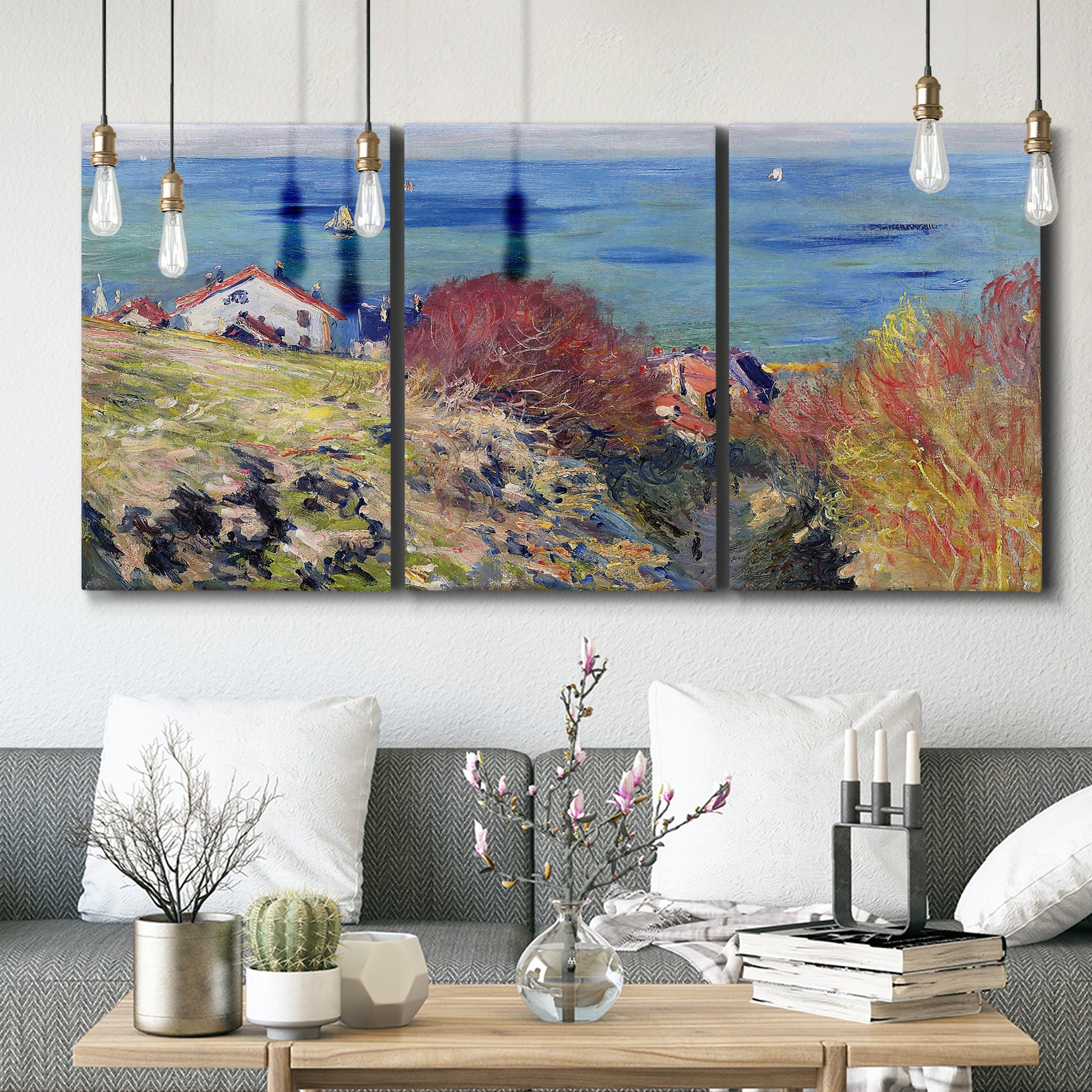 Three-panel canvas wall art featuring coastal village shoreline landscape, displayed in a modern living room above seating.
