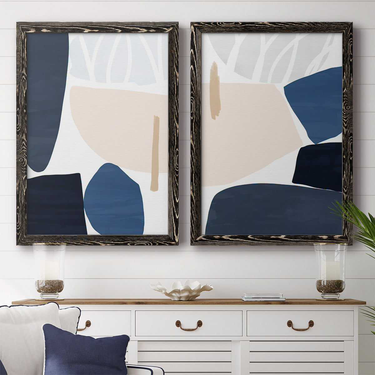 Set of two black barnwood framed canvas prints depicting a coordinated art pair of large navy cream and beige organic geometric shapes rendered as minimalist color-block abstracts above a dining room sideboard.
