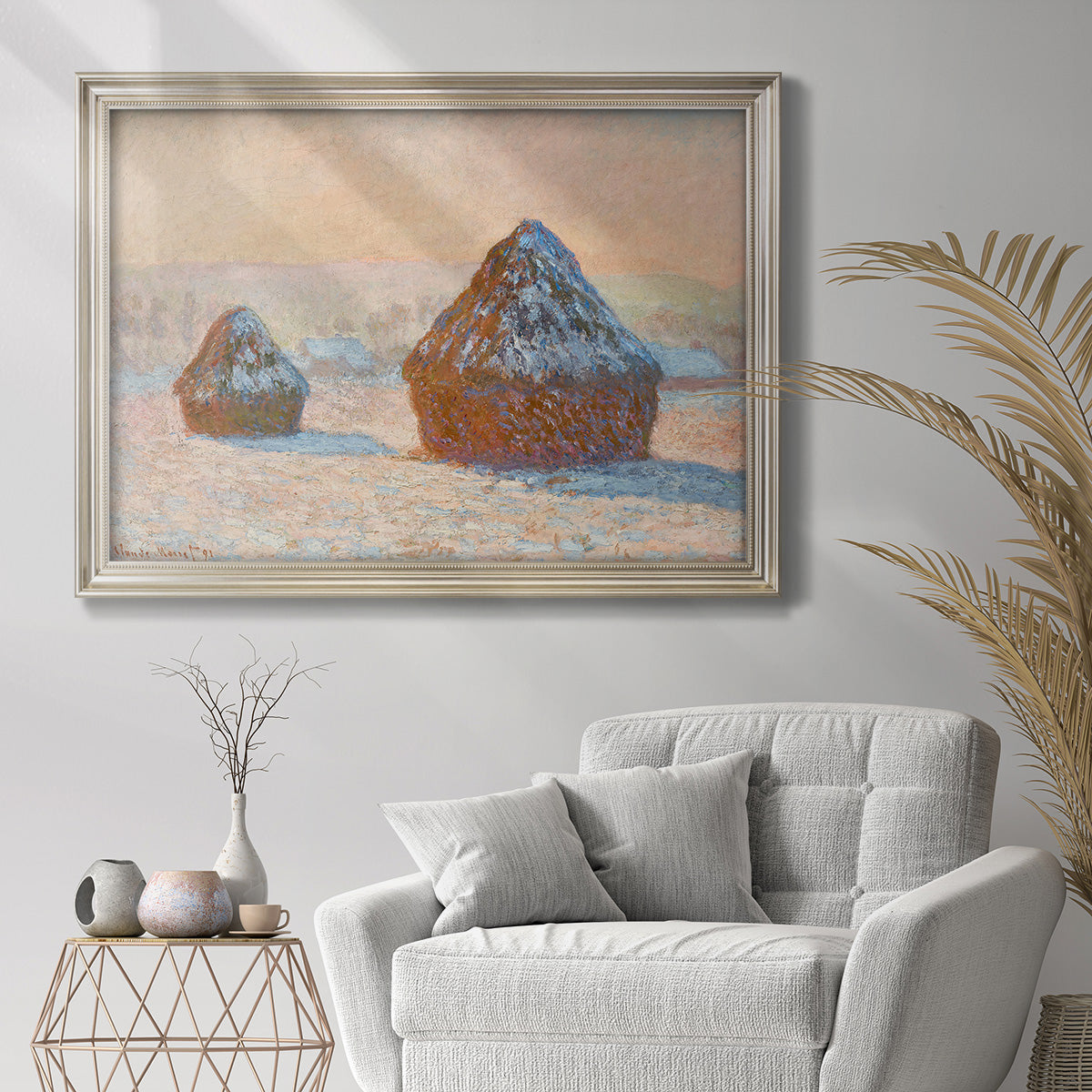 Impressionist winter haystack scene by Claude Monet in an ornate champagne frame displayed in a bright interior setting.