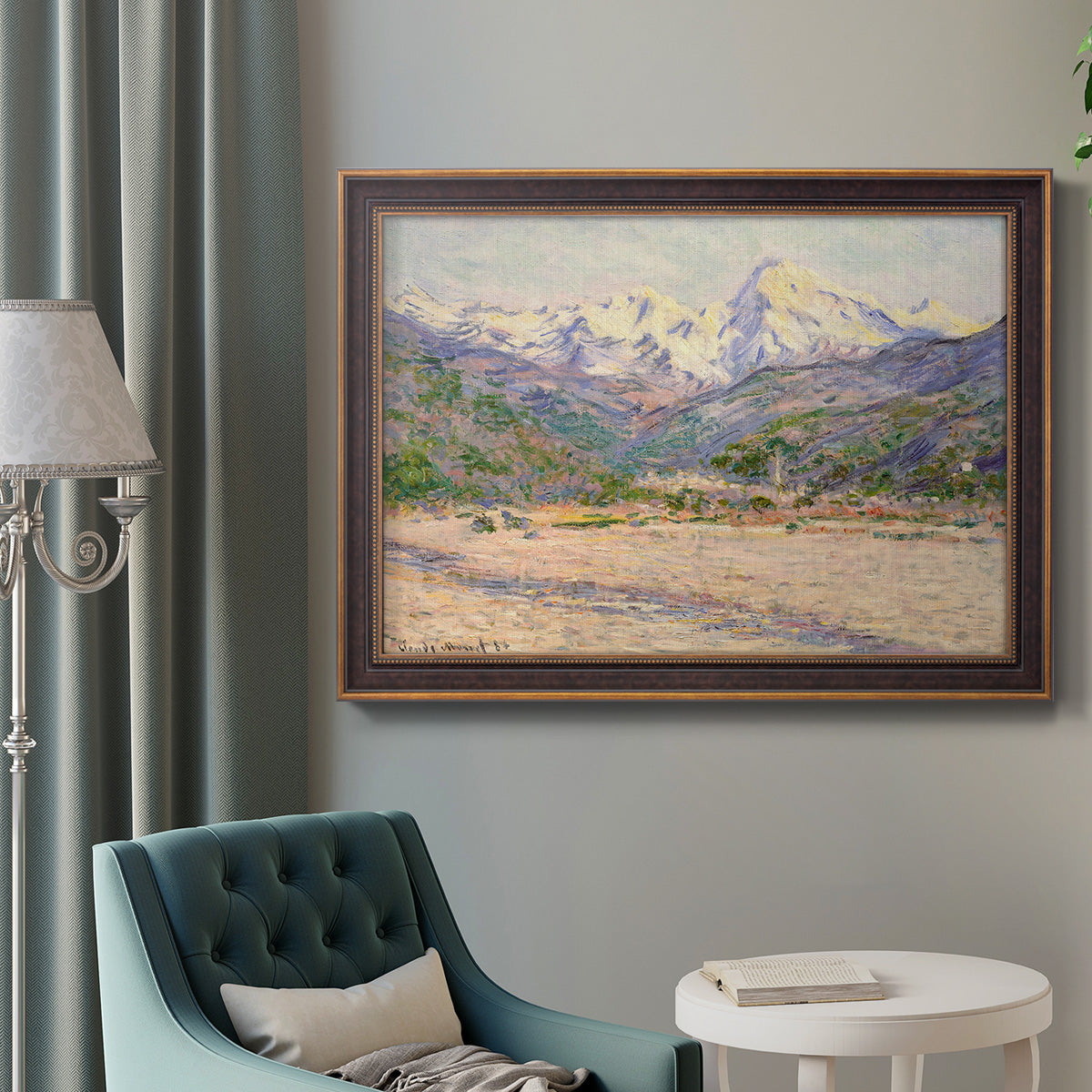 Impressionist valley landscape in southern France by Claude Monet in an ornate bronzed mahogany wood frame displayed in a bright interior setting.
