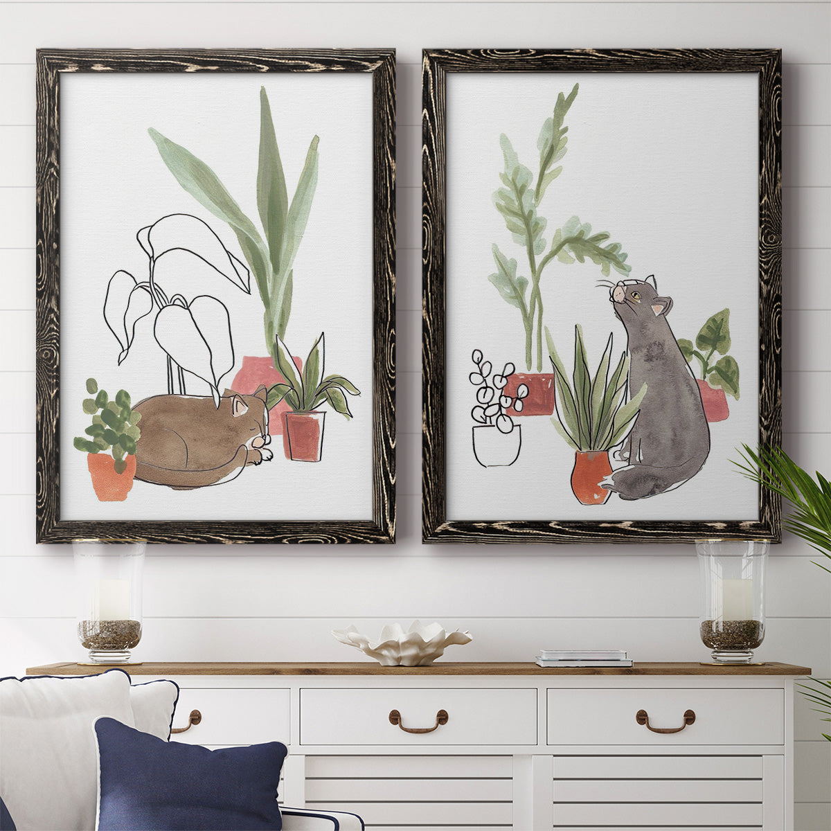 Set of two black barnwood framed canvas prints depicting a coordinated art pair of cats tucked among collections of potted houseplants rendered as whimsical botanical animal illustrations above a dining room sideboard.