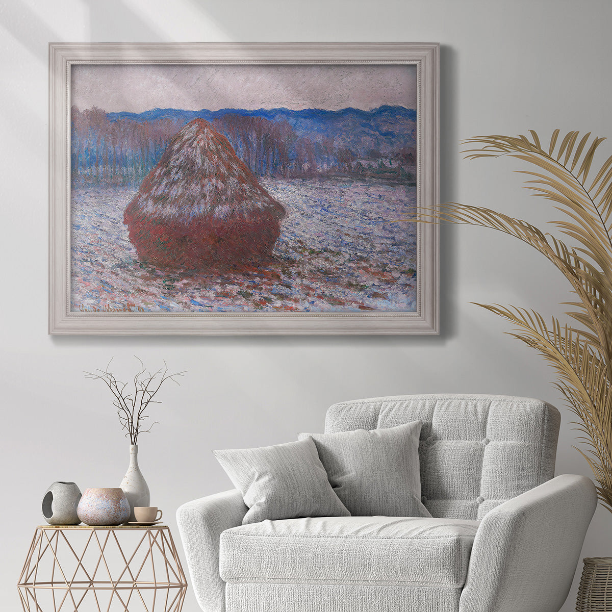 Impressionist single haystack landscape by Claude Monet in an ornate weathered white frame displayed in a bright interior setting.