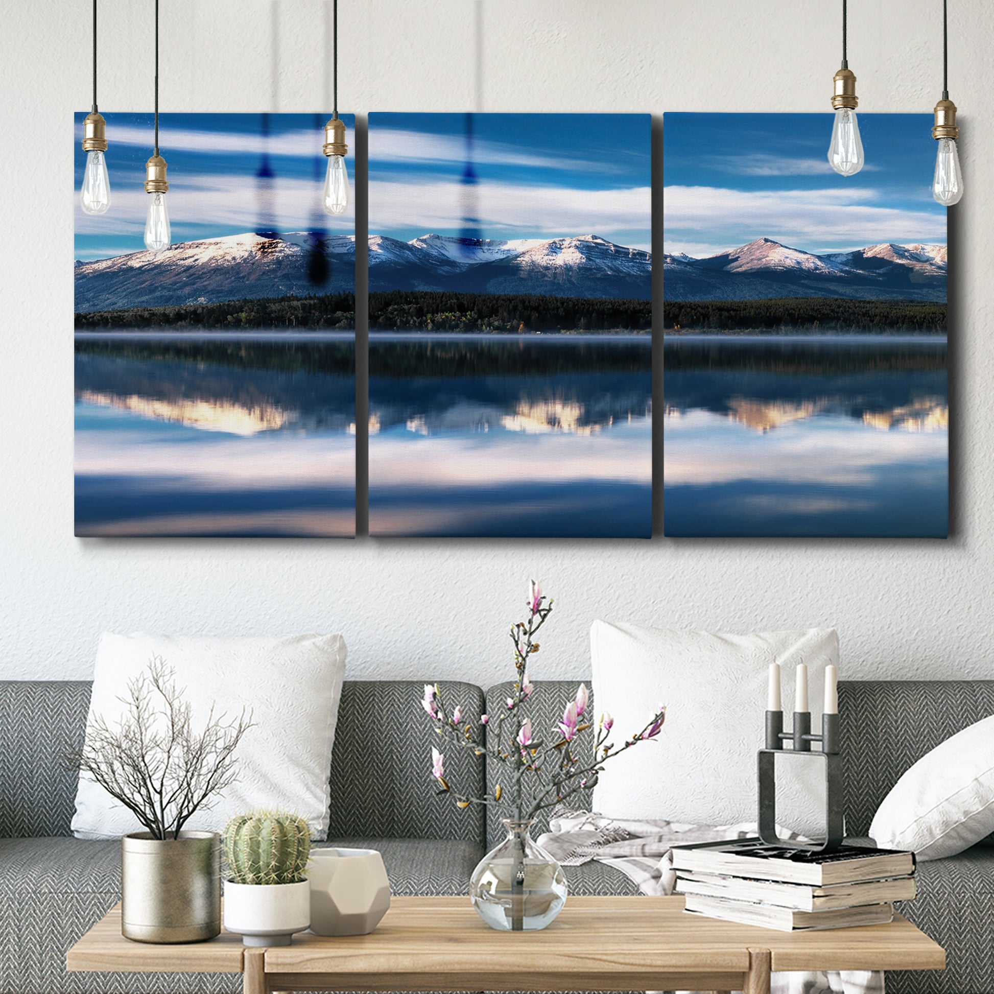 Three-panel canvas wall art featuring calm lake beneath mountains photograph, displayed in a modern living room above seating.