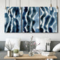 Three-panel canvas wall art featuring flowing blue watercolor wave forms, displayed in a modern living room above seating.