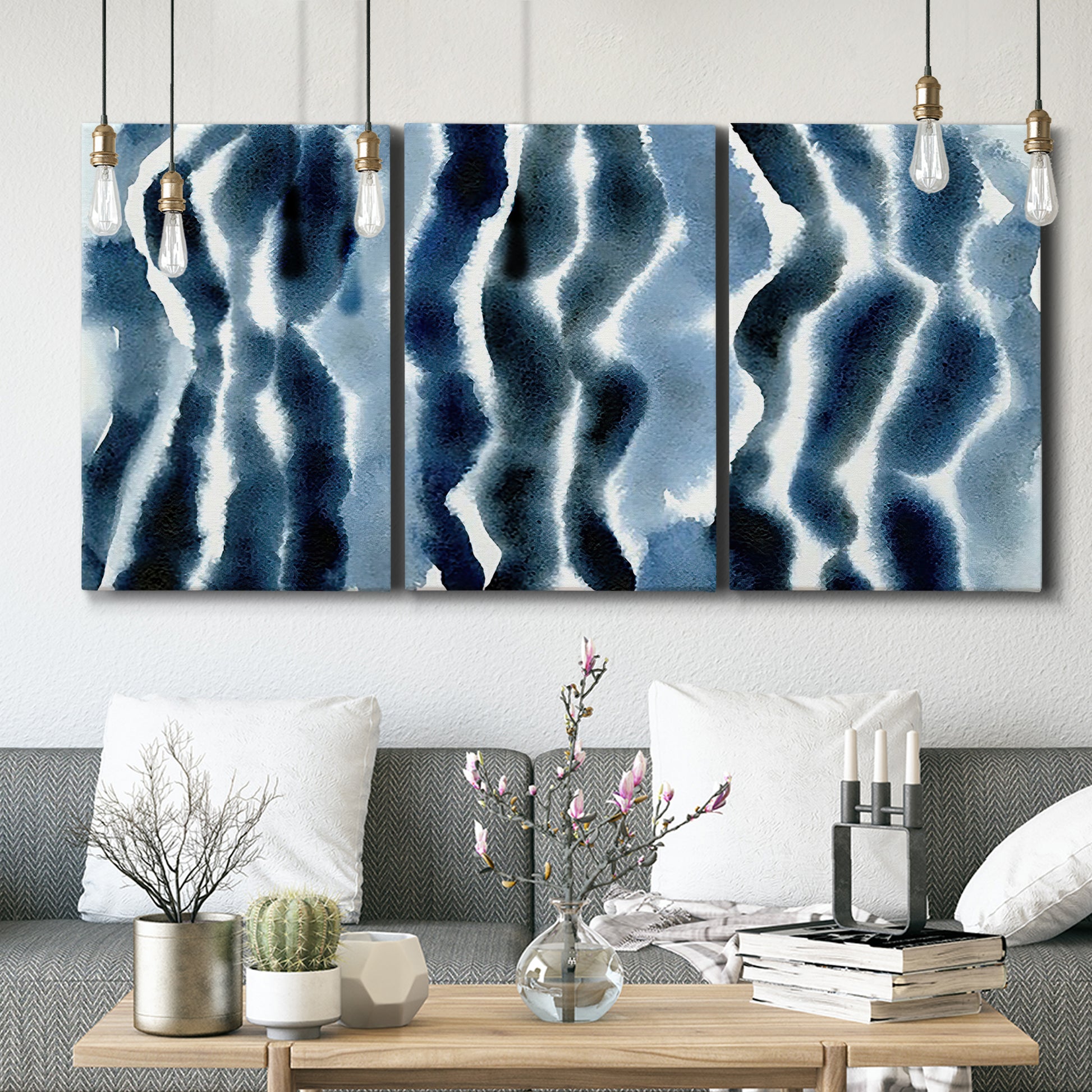 Three-panel canvas wall art featuring flowing blue watercolor wave forms, displayed in a modern living room above seating.