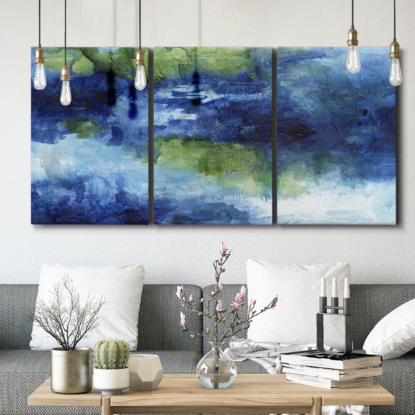 Three-panel canvas wall art featuring flowing blue abstract watercolor, displayed in a modern living room above seating.
