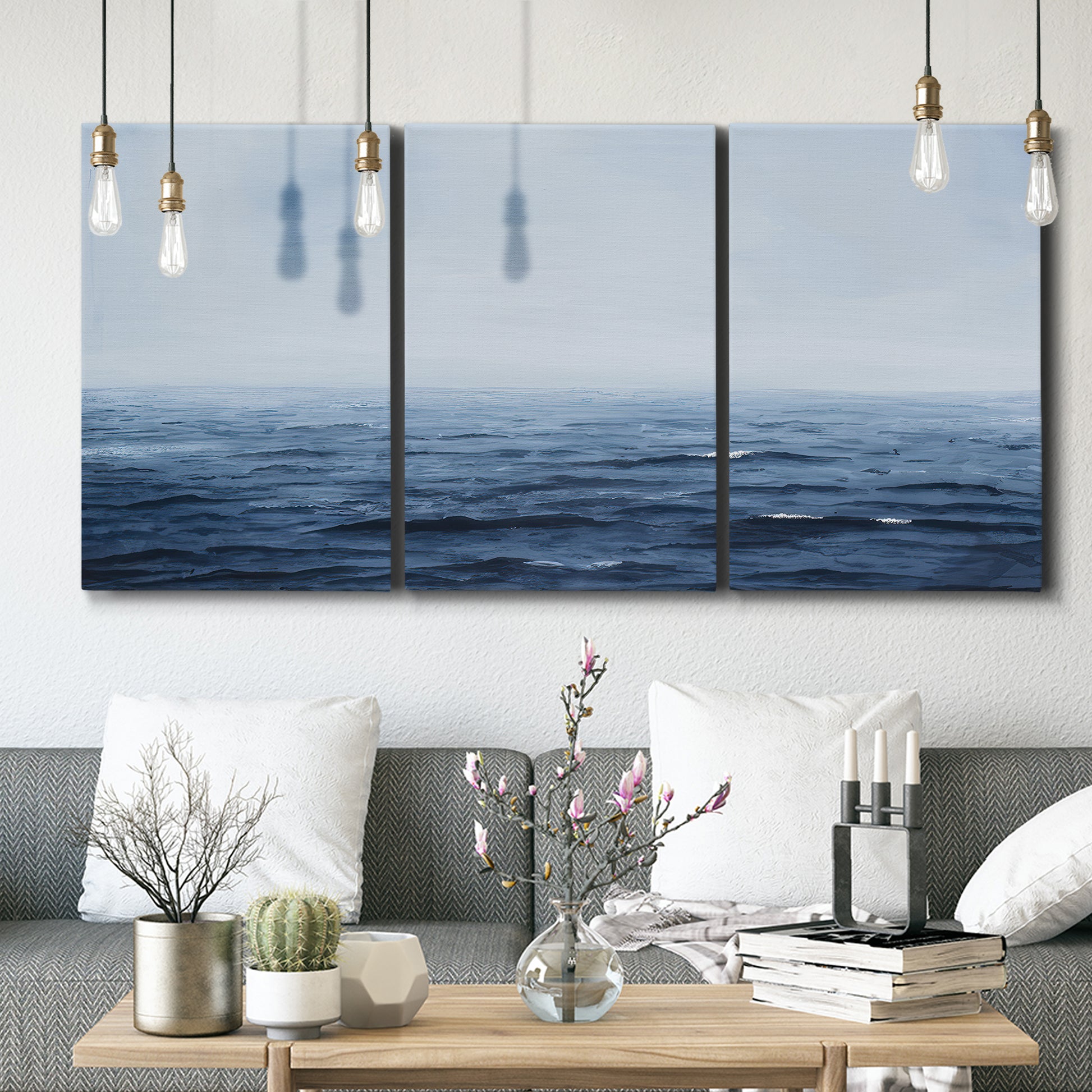 Three-panel canvas wall art featuring grayscale seascape with horizon, displayed in a modern living room above seating.
