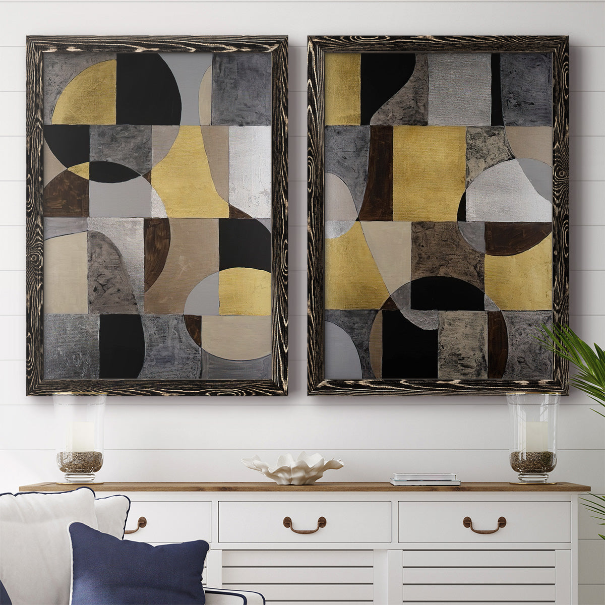 Set of two black barnwood framed canvas prints depicting a coordinated art pair of interlocking black gray cream and gold geometric sections rendered as structured modern abstracts above a dining room sideboard.