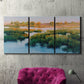 Three-panel canvas wall art featuring pastoral marshland landscape, displayed in a living room above a suede accent chair.