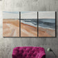 Three-panel canvas wall art featuring abstract coastal beach composition, displayed in a living room above a suede accent chair.