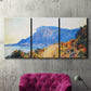 Three-panel canvas wall art featuring winding red road hillside, displayed in a living room above a suede accent chair.