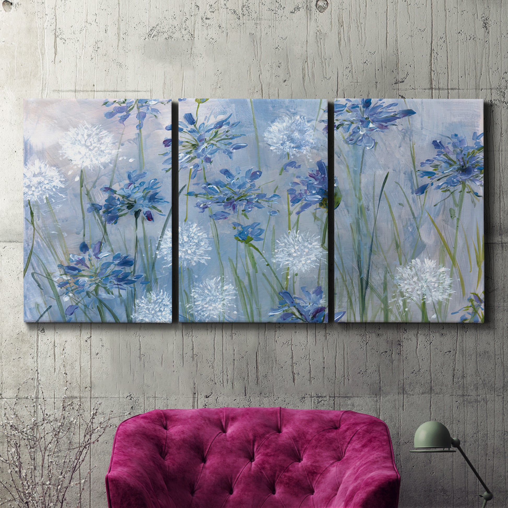 Three-panel canvas wall art featuring delicate watercolor floral blooms, displayed in a living room above a suede accent chair.